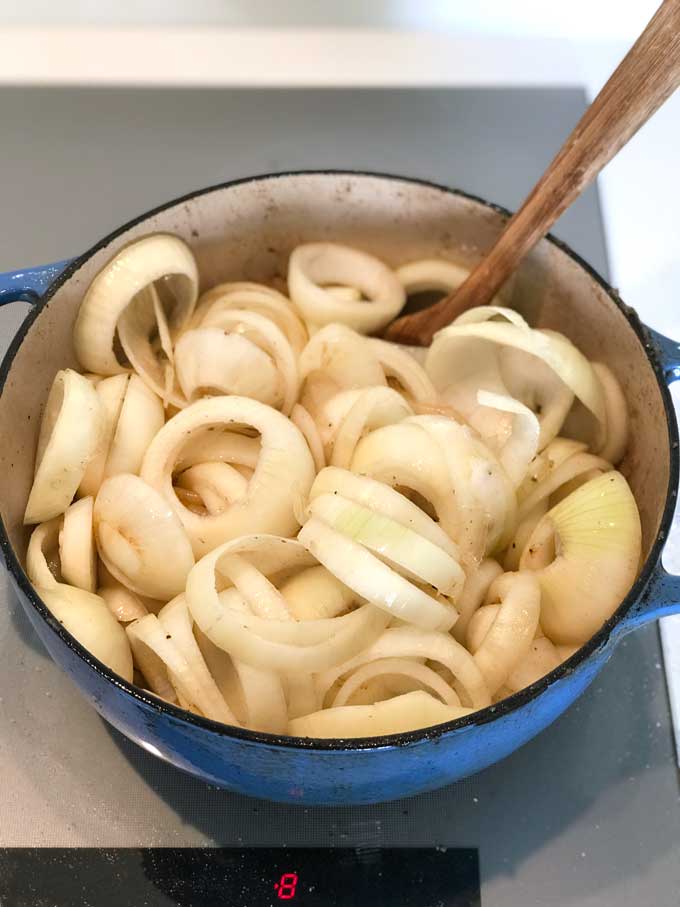 Blue Dutch oven filled to the brim with thickly sliced rings of raw onions