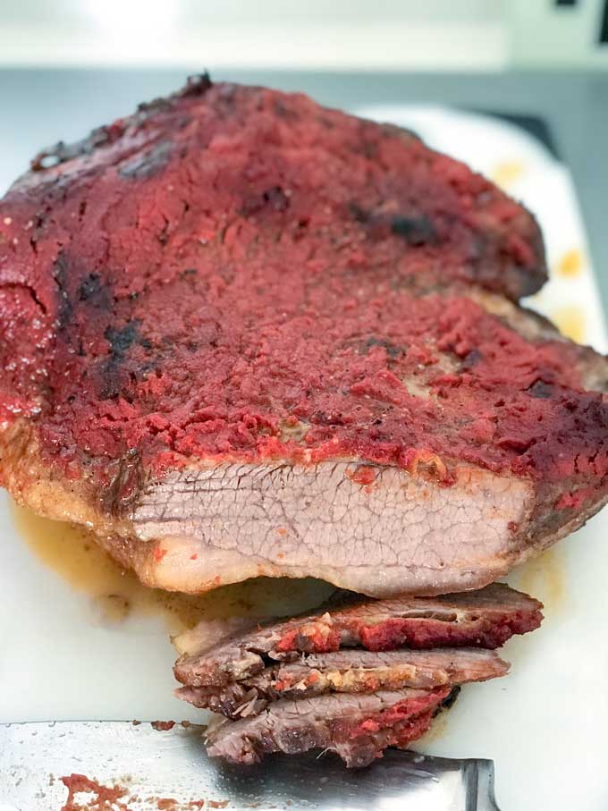 Close up of a tomato-paste coated half-cooked brisket of beef being sliced across the grain