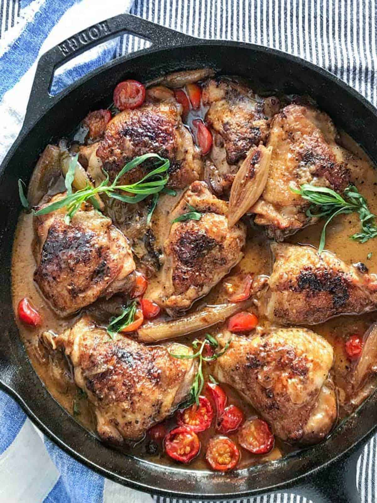 8 oven braised chicken thighs in a cast iron skillet with cherry tomatoes, shallots and sprigs of tarragon