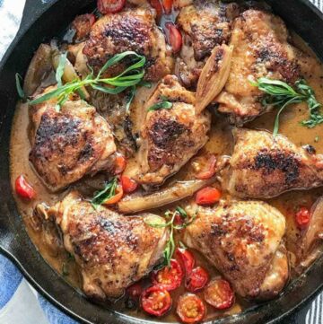 5 braised chicken thighs in a cast iron skillet with cherry tomatoes, shallots and sprigs of tarragon