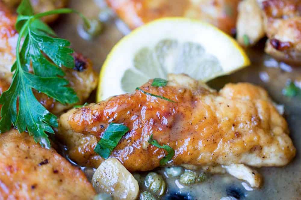 close up of a chicken tender piccata with a half lemon slice and a sprinkle of parsley