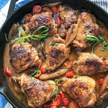 cast iron skillet with 8 braised chicken thighs in mustard wine sauce with sliced cherry tomatoes and sprigs of tarragon