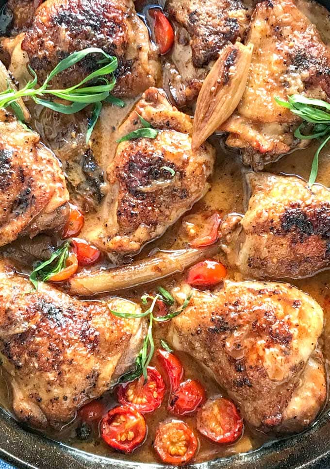 cast iron skillet with 8 braised chicken thighs in mustard wine sauce with sliced cherry tomatoes and sprigs of tarragon