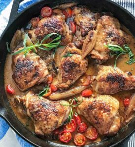 8 braised chicken thighs in a cast iron skillet with cherry tomatoes, shallots and tarragon