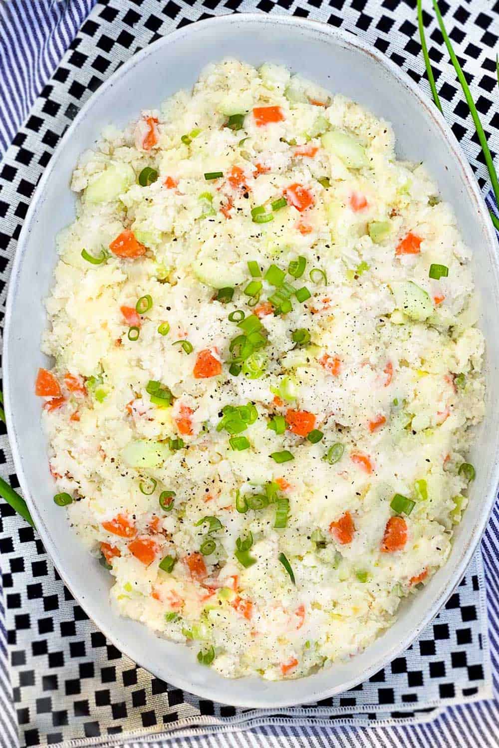 Oval serving bowl filled with Japanese Potato Salad, on a white dish towel with black squares.