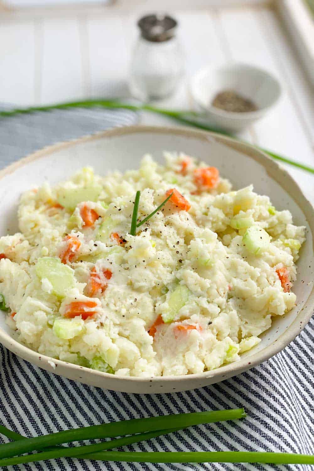 oval bowl filled with Japanese potato salad, salt shaker and small bowl of pepper in the background