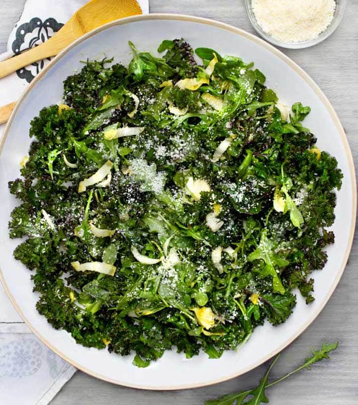 Big green salad in a white bowl with a side dish of parmesan cheese