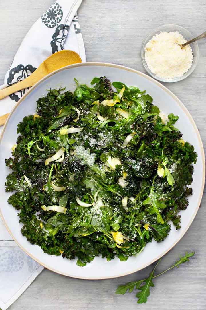 Big green salad in a white bowl with a side dish of parmesan cheese