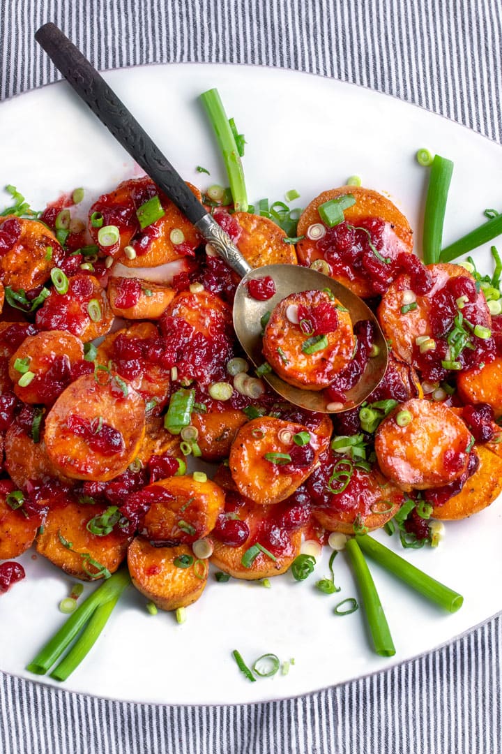white platter with roasted sweet potatoes topped with cranberry maple citrus glaze and chopped scallions
