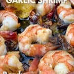 half a dozen sautéd shrimp in a skillet with olive oil and a sliced of baguette being dipped into the oil