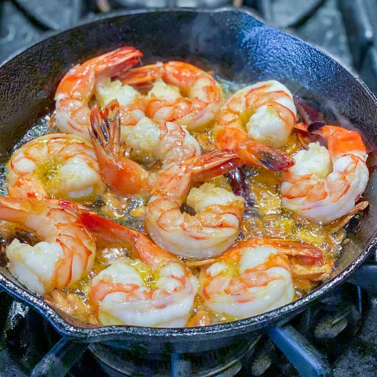 Ten shrimp sautéing in oil, in a small cast iron skillet.