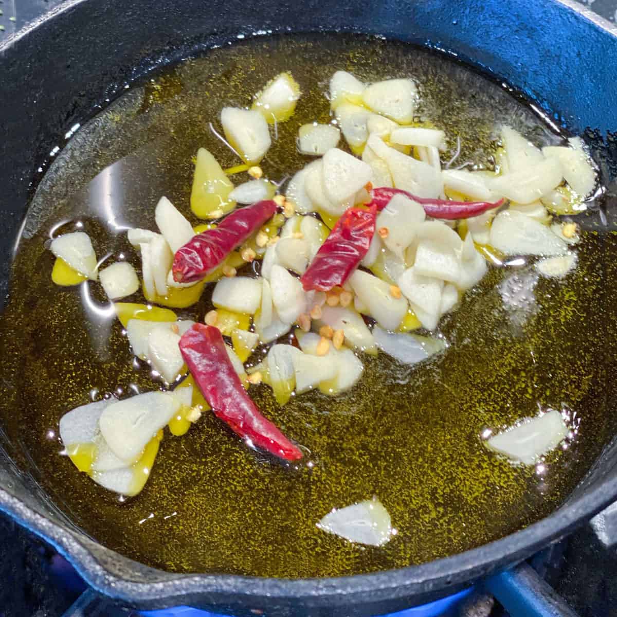 lots of sliced garlic and three small red chilies in a small cast iron pan with lots of olive oil.