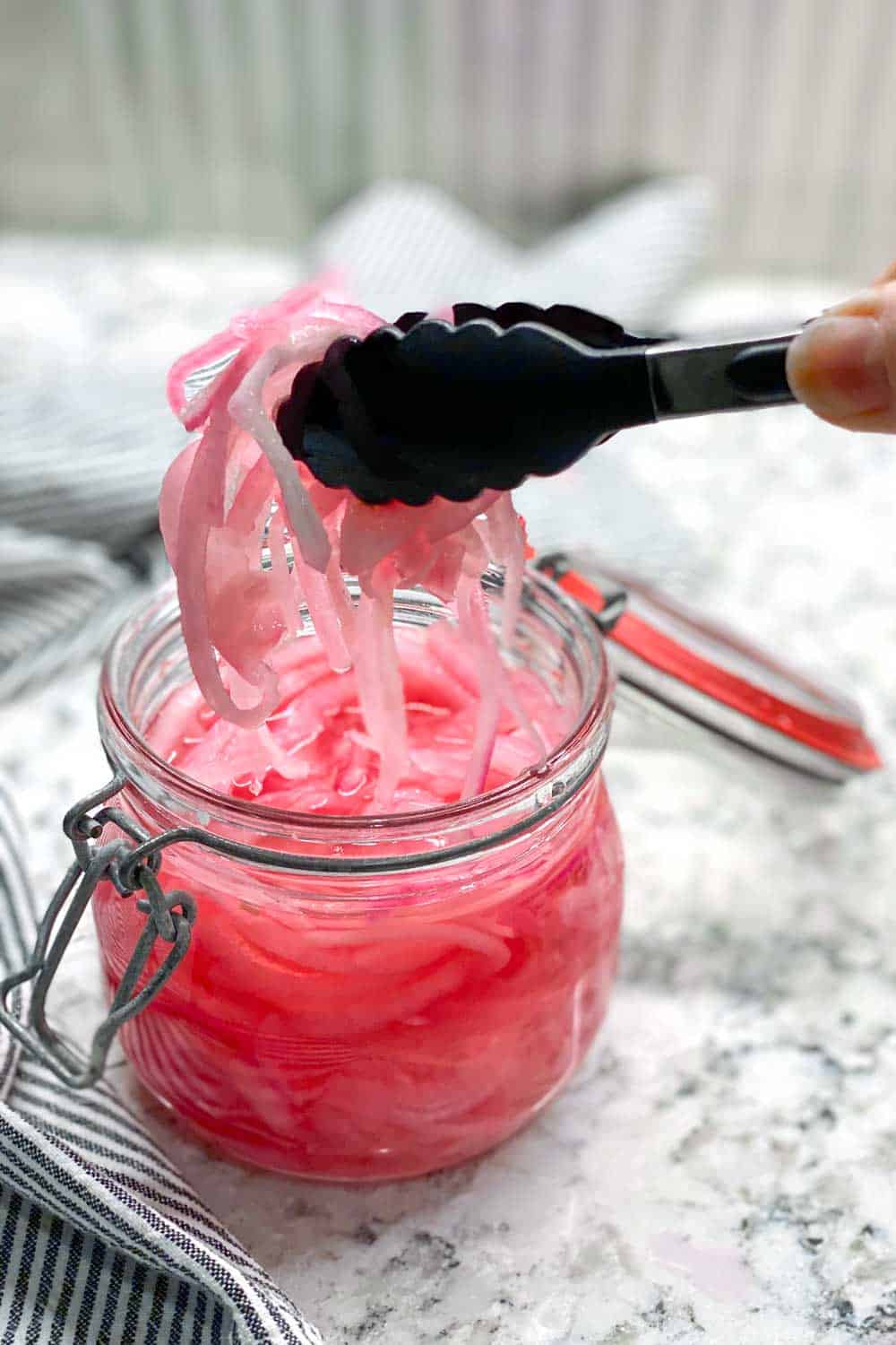 glass jar filled with pickled red onions, tongs lifting out a bunch of the onions