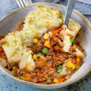 bowl of cooked ground beef with corn and peas in sauce topped with fluffy mashed potatoes.
