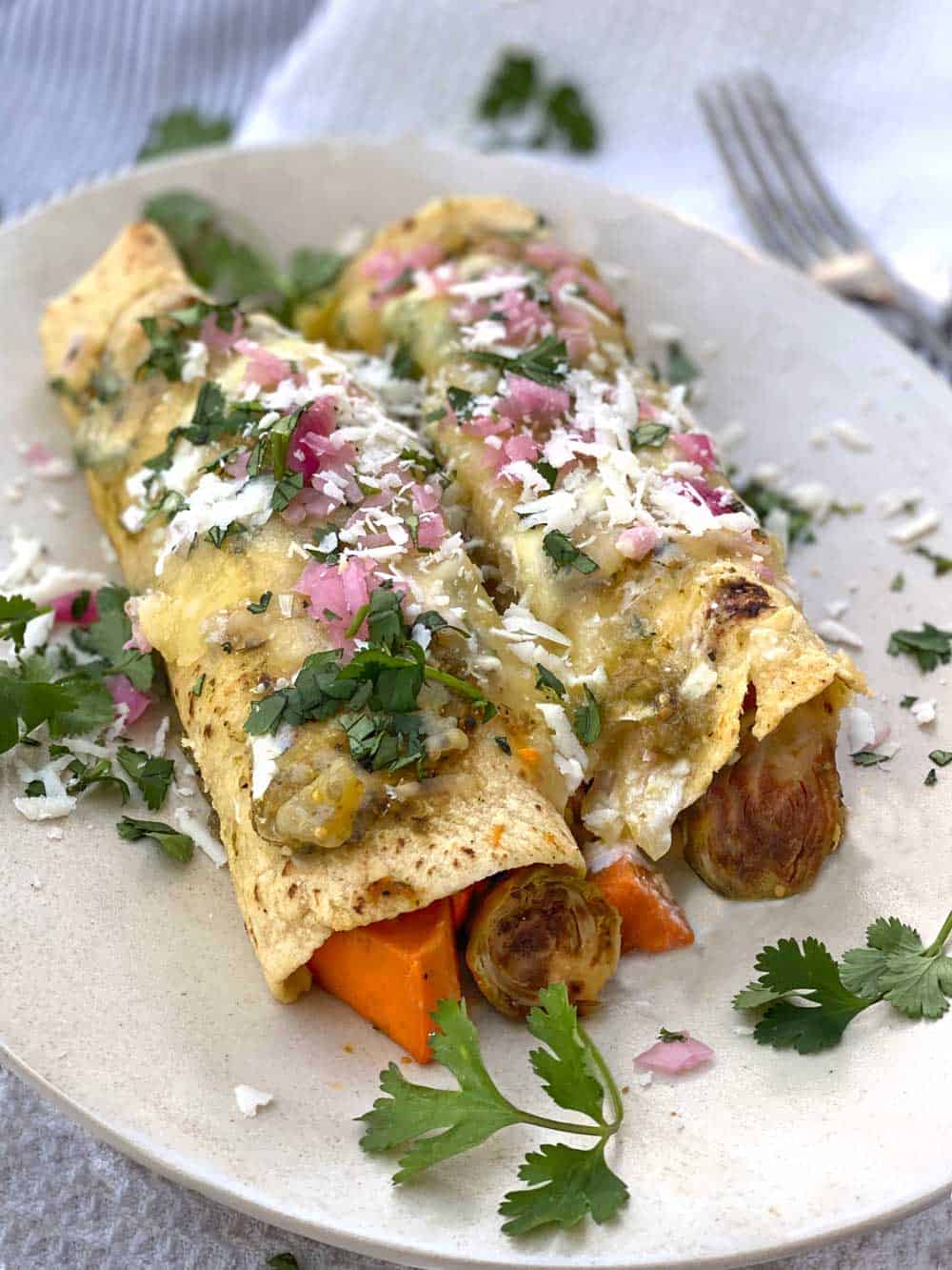 two vegetarian enchiladas on a white plate garnished with shredded white chese, cilantro and chopped red onion 