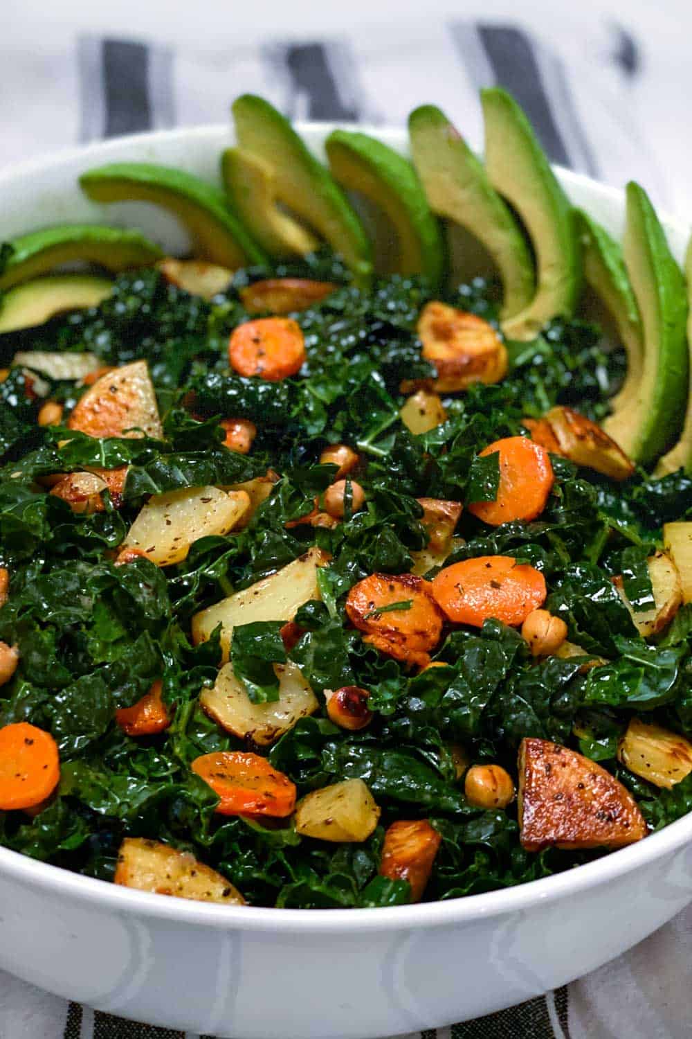 close up of white serving bowl filled with shredded kale and roasted carrots, potatoes, chickpeas and sliced avocado