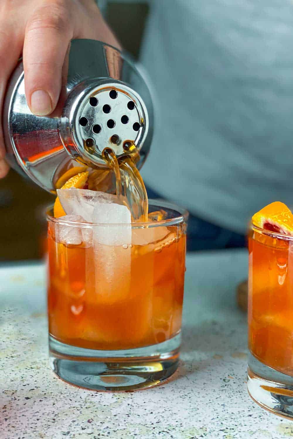 How to make a paper plane cocktail, pouring it out of a shaker into two tumblers filled with ice