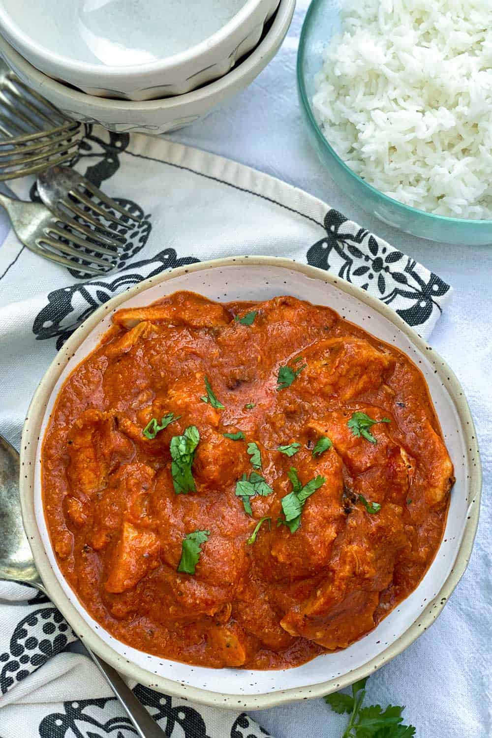 a big bowl of chicken ruby, Indian chicken curry, with a bowl of rice on the side, some forks, and some bowls.