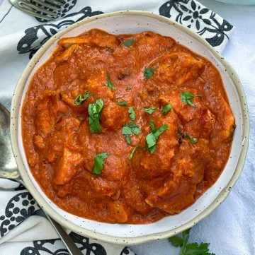 White bowl filled with Chicken Ruby, vibrant tomato-based Indian chicken curry, sprinkled with chopped cilantro