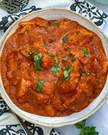 White bowl filled with Chicken Ruby, vibrant tomato-based Indian chicken curry, sprinkled with chopped cilantro