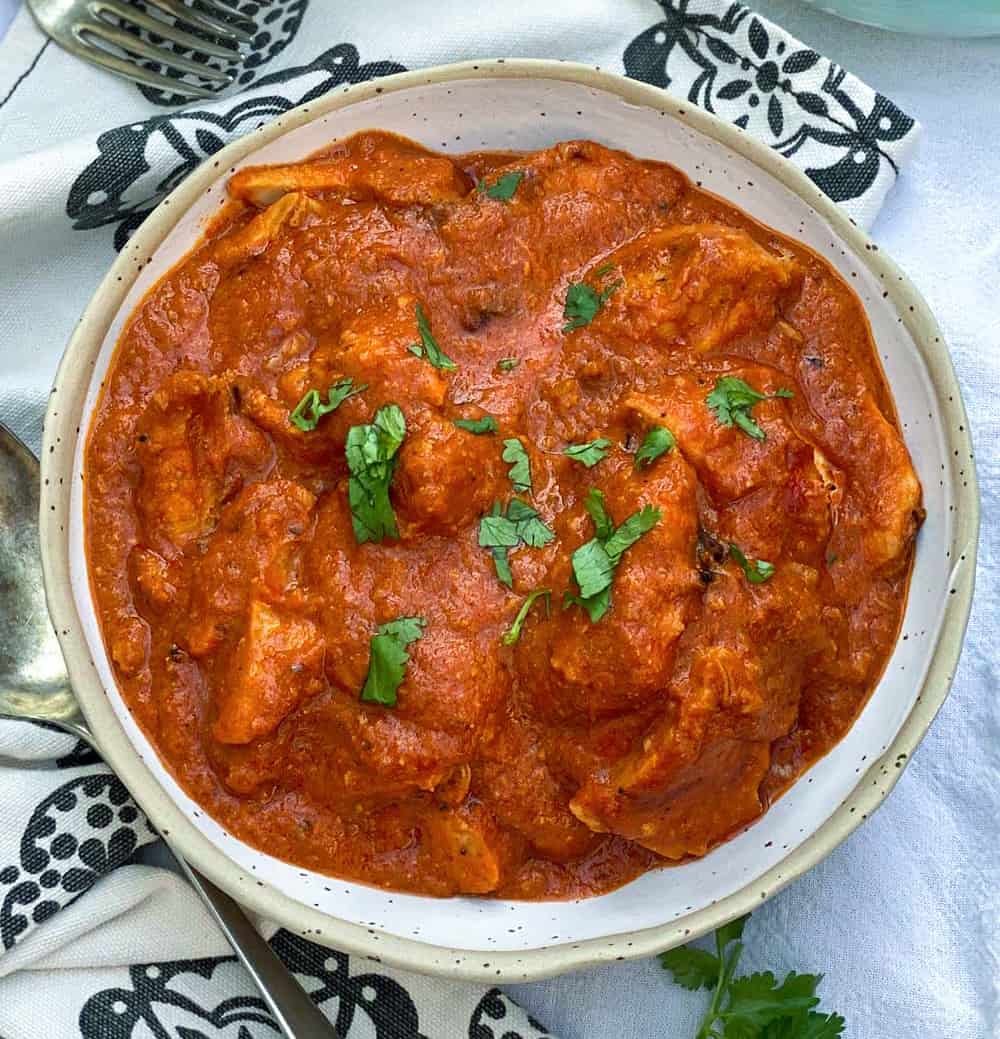 White bowl filled with Chicken Ruby, vibrant tomato-based Indian chicken curry, sprinkled with chopped cilantro