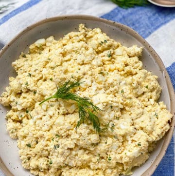 egg salad in a white bowl with a sprig of dill in the middle