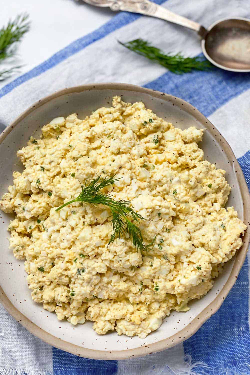 egg salad in a white bowl with a sprig of dill in the middle