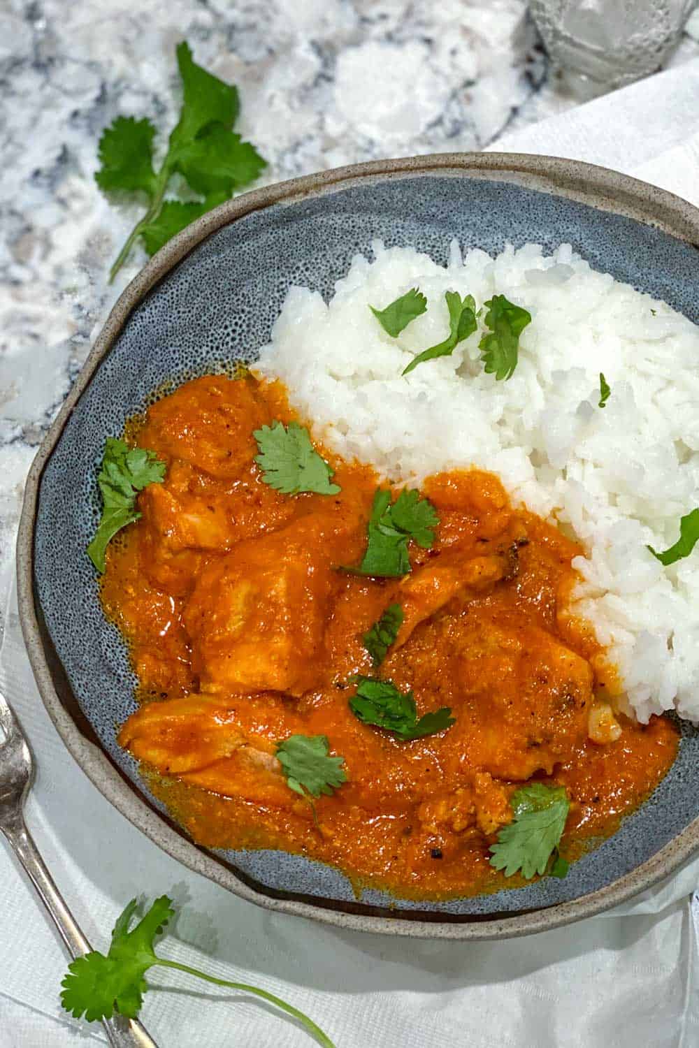 Indian ruby chicken curry in a blue bowl with rice, sprinkled with chopped cilantro