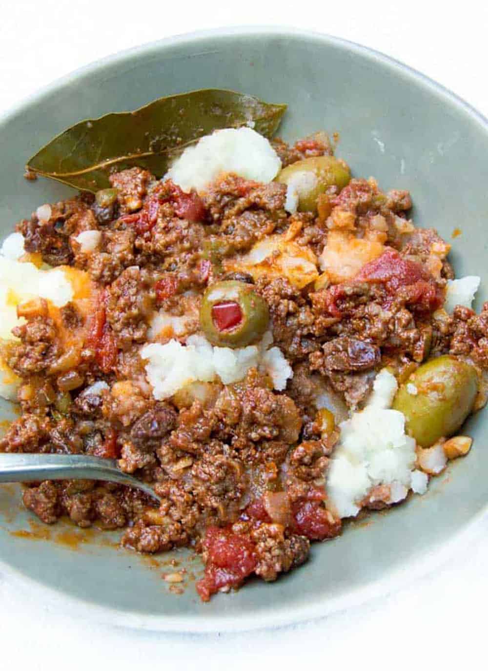 overhead shot of a light blue bowl filled with Cuban picadillo on top of mashed potatoes