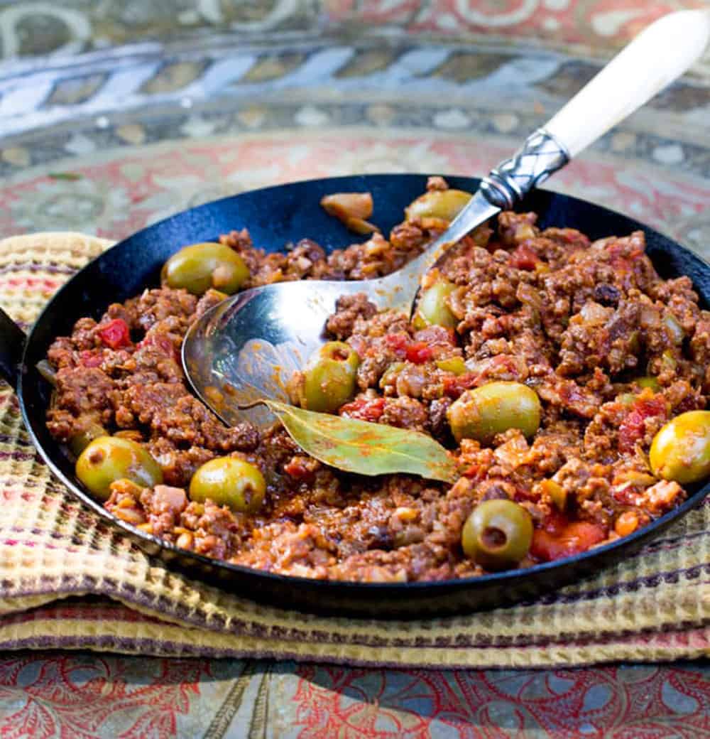 Black cast iron skillet filled with Cuban picadillo: ground beef stew with olives