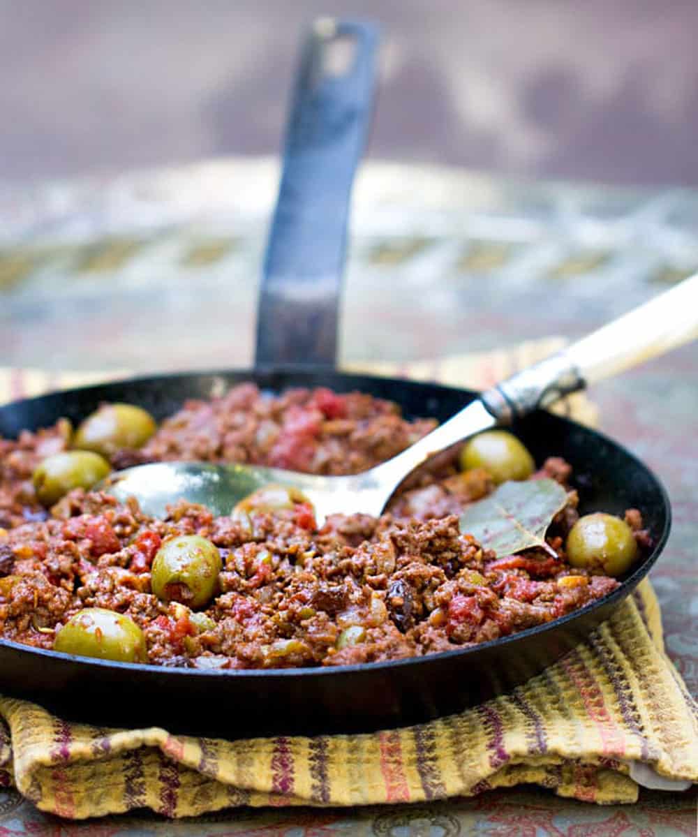 Black cast iron skillet filled with Cuban picadillo: ground beef stew with olives