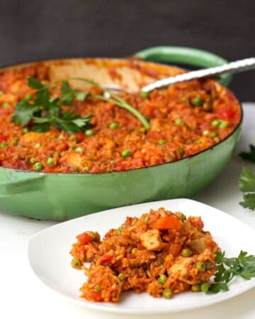 jollof rice in a light green round Dutch oven with a sprig of parsley on top, plus a small white plate with a portion of jollof rice on it