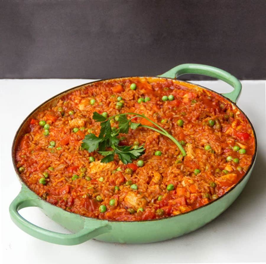 jollof rice in a light green round Dutch oven with a sprig of parsley on top