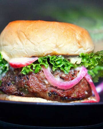 close up of a Korean bbq burger in a bun with green leaf lettuce peeking out and a strip of pickled red onion draping down