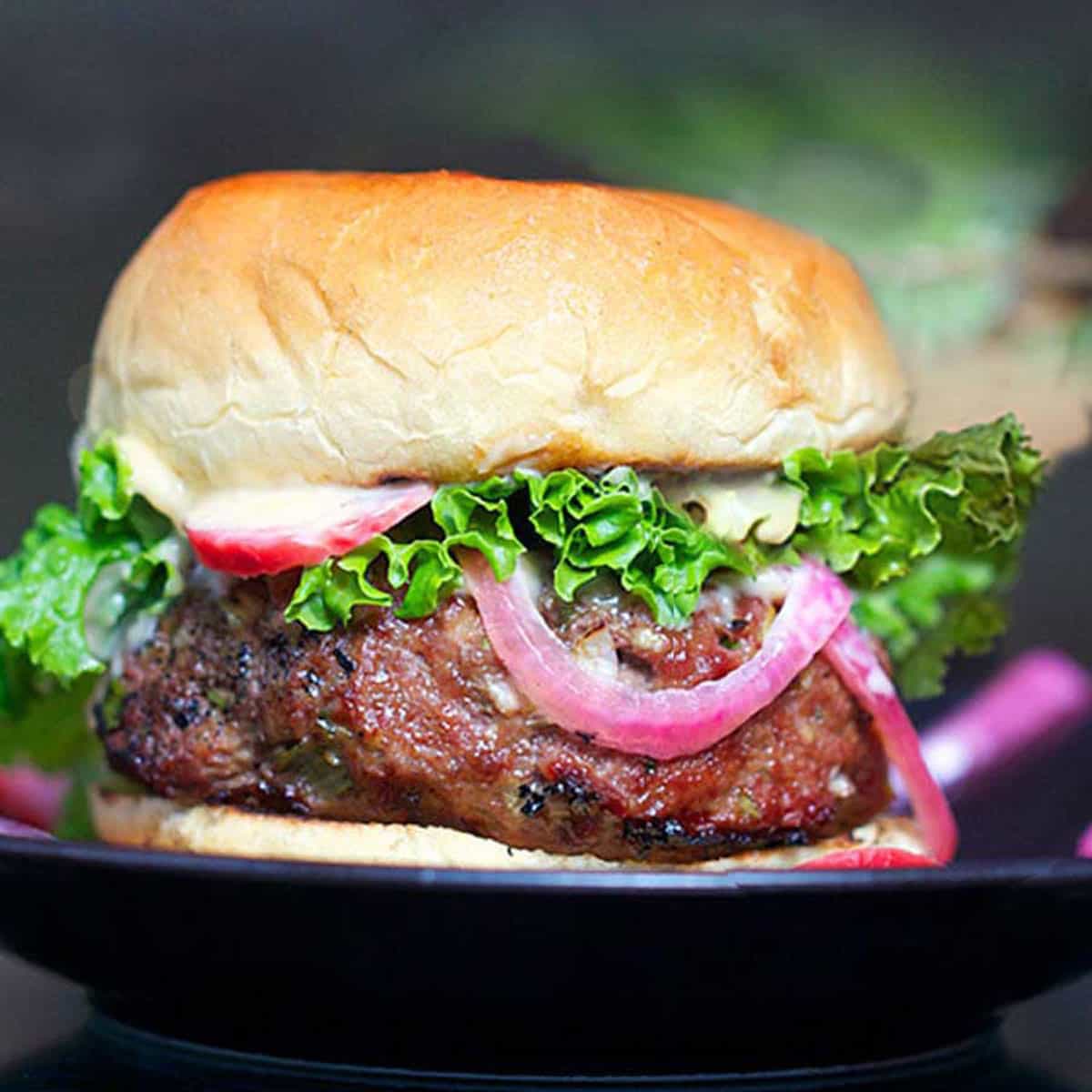 close up of a Korean bbq burger in a bun with green leaf lettuce peeking out and a strip of pickled red onion draping down