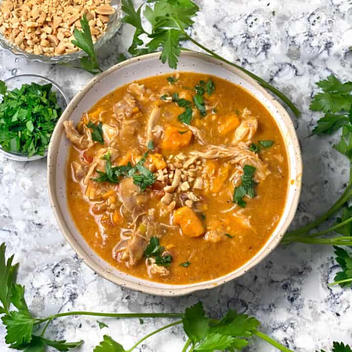 West African peanut stew with chicken and sweet potatoes in a bowl, surrounded by sprigs of parsley.
