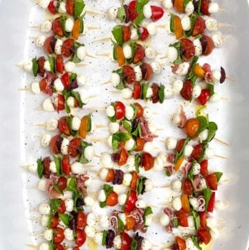 3 dozen mini caprese skewers on a white tray, with tomatoes, basil leaves and mini mozzarella balls