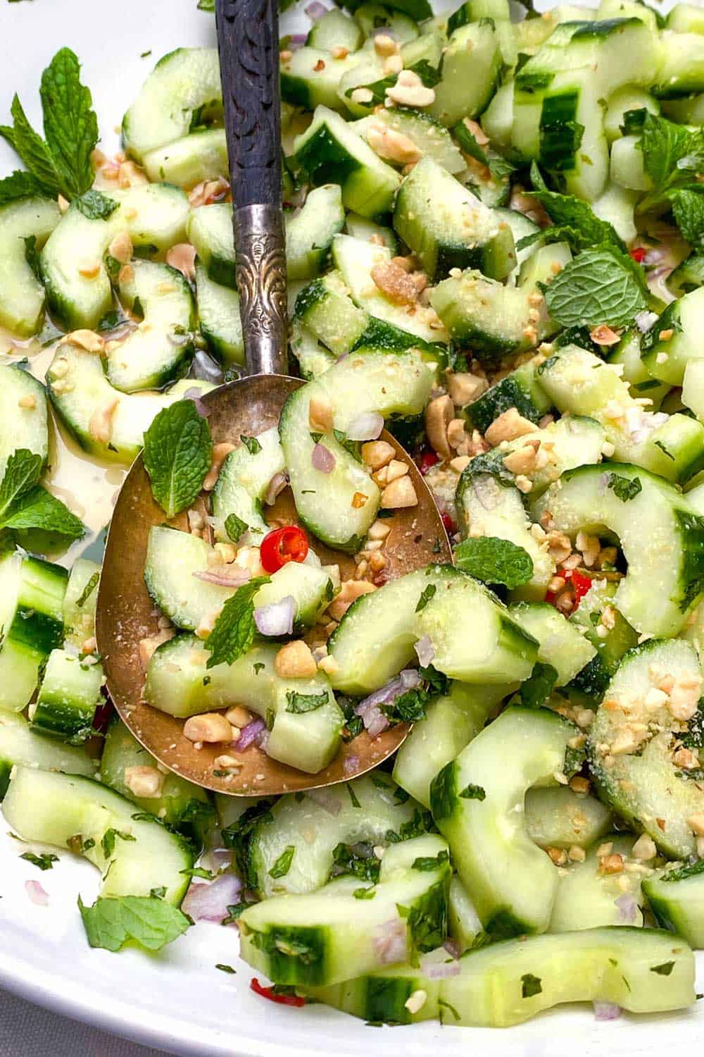 close up of Thai cucumber salad: sliced cucumber moons with lim dressing, bits of chopped mint, chopped peanuts and red Thai chili peppers.