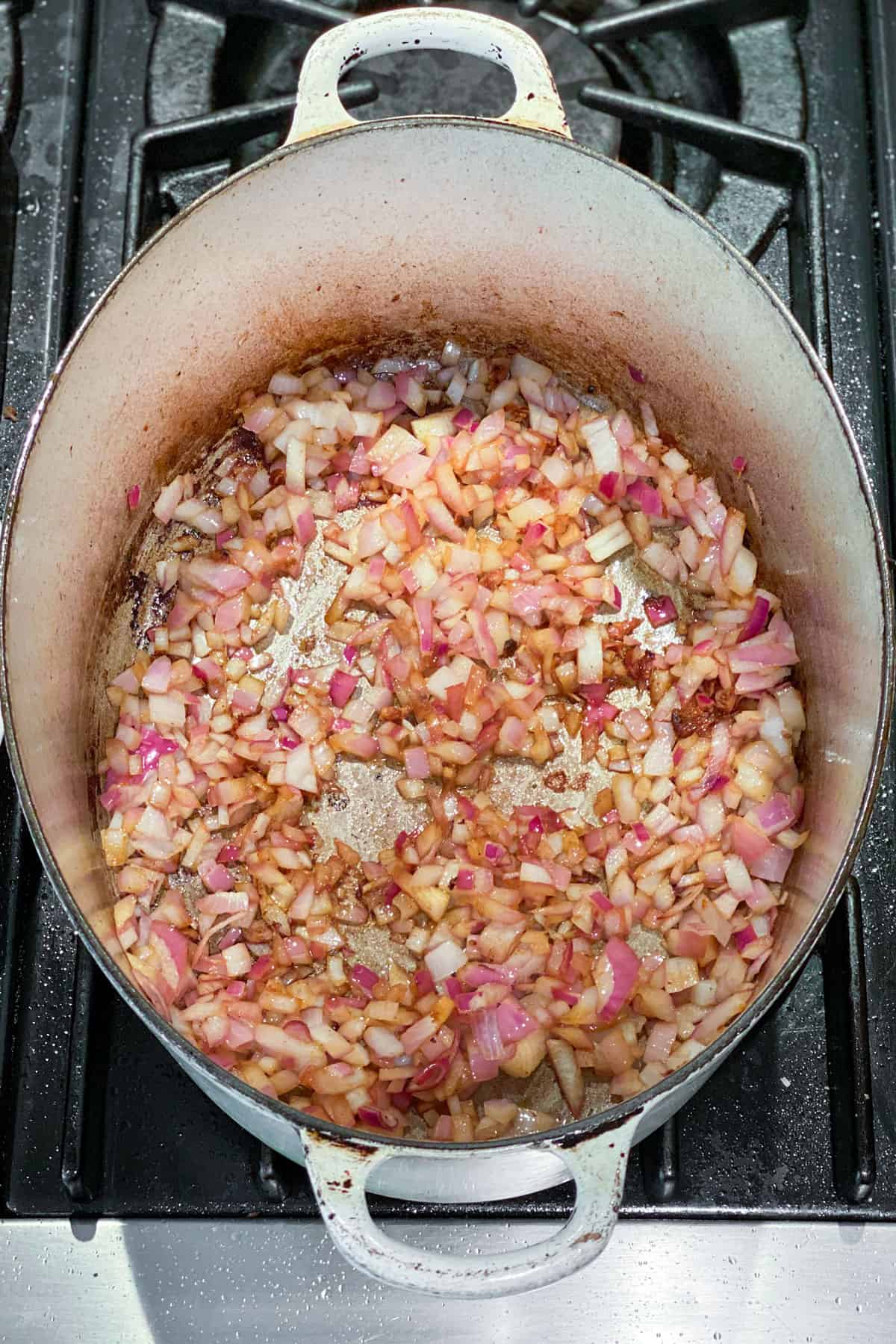 Oval dutch oven filled with chopped red onion and garlic, browning.