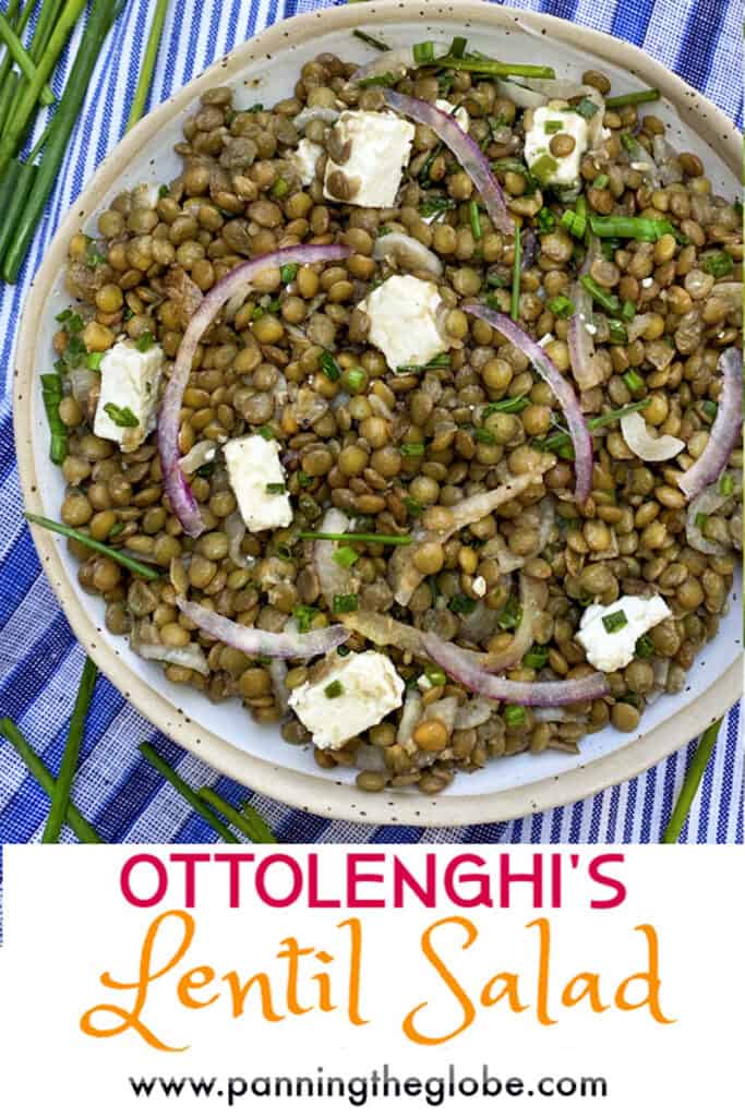 a white bowl filled with lentil salad and cubes of feta, on a blue striped dish towel with some fresh chives on the side