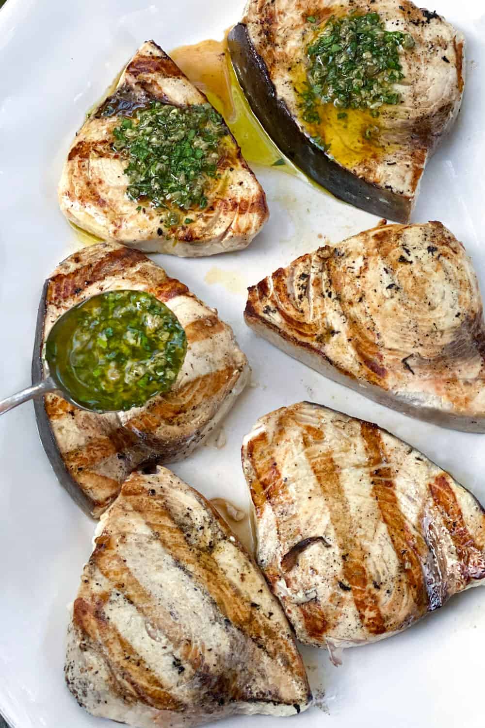 6 grilled swordfish steaks on a white platter, three are topped with salsa verde