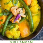 Vibrant sri lankan vegetable curry of sweet potatoes, cauliflower and green beans, in a black bowl.