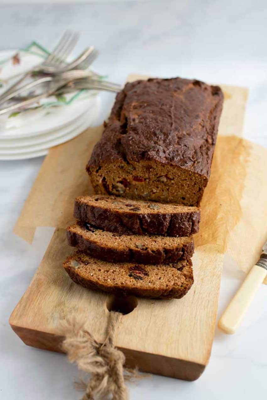 a loaf of pumpkin bread with three slices cut, atop a long wooden cuting board