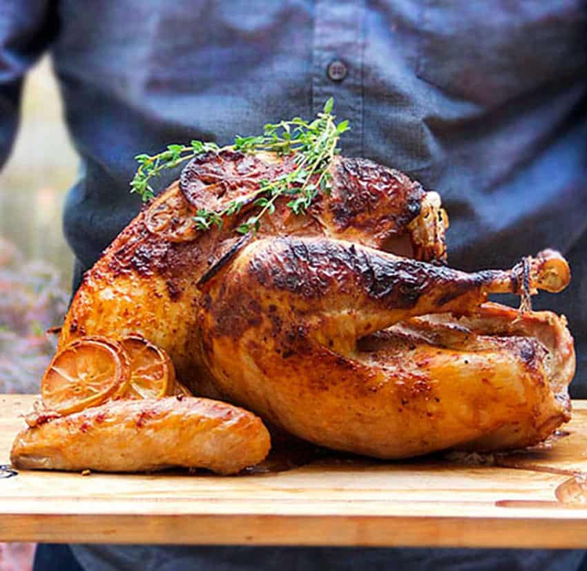 large cooked turkey on a light wooden board with a sprig of thyme on top