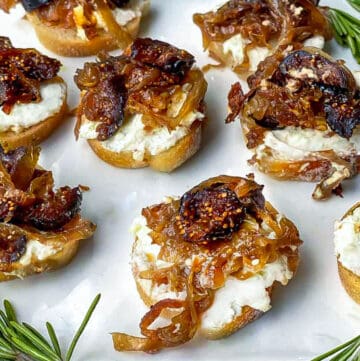 7 fig and goat cheese crostini on a platter with sprigs of rosemary around the plate