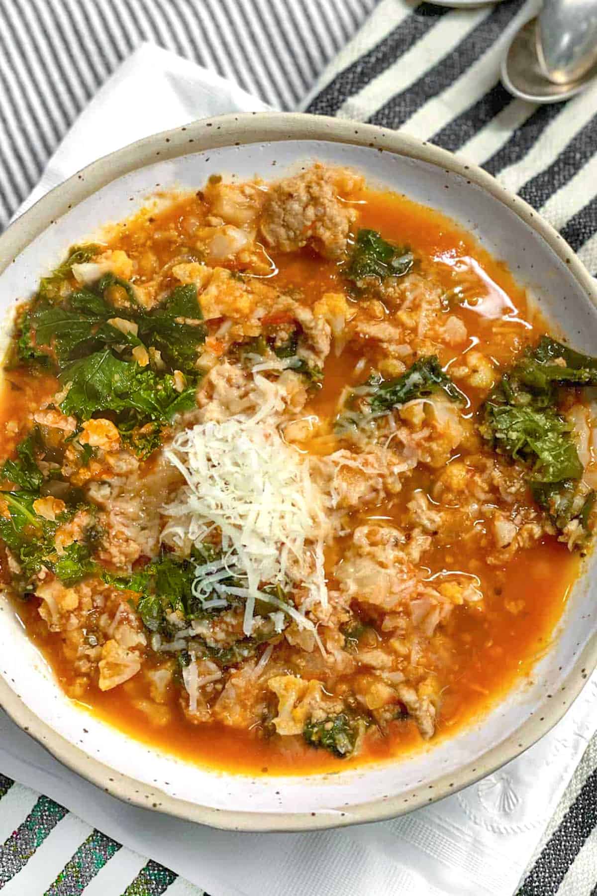 Ceramic bowl filled with tomato based soup that has lots of ground turkey, chopped cauliflower and kale. Topped with grated parmesan.