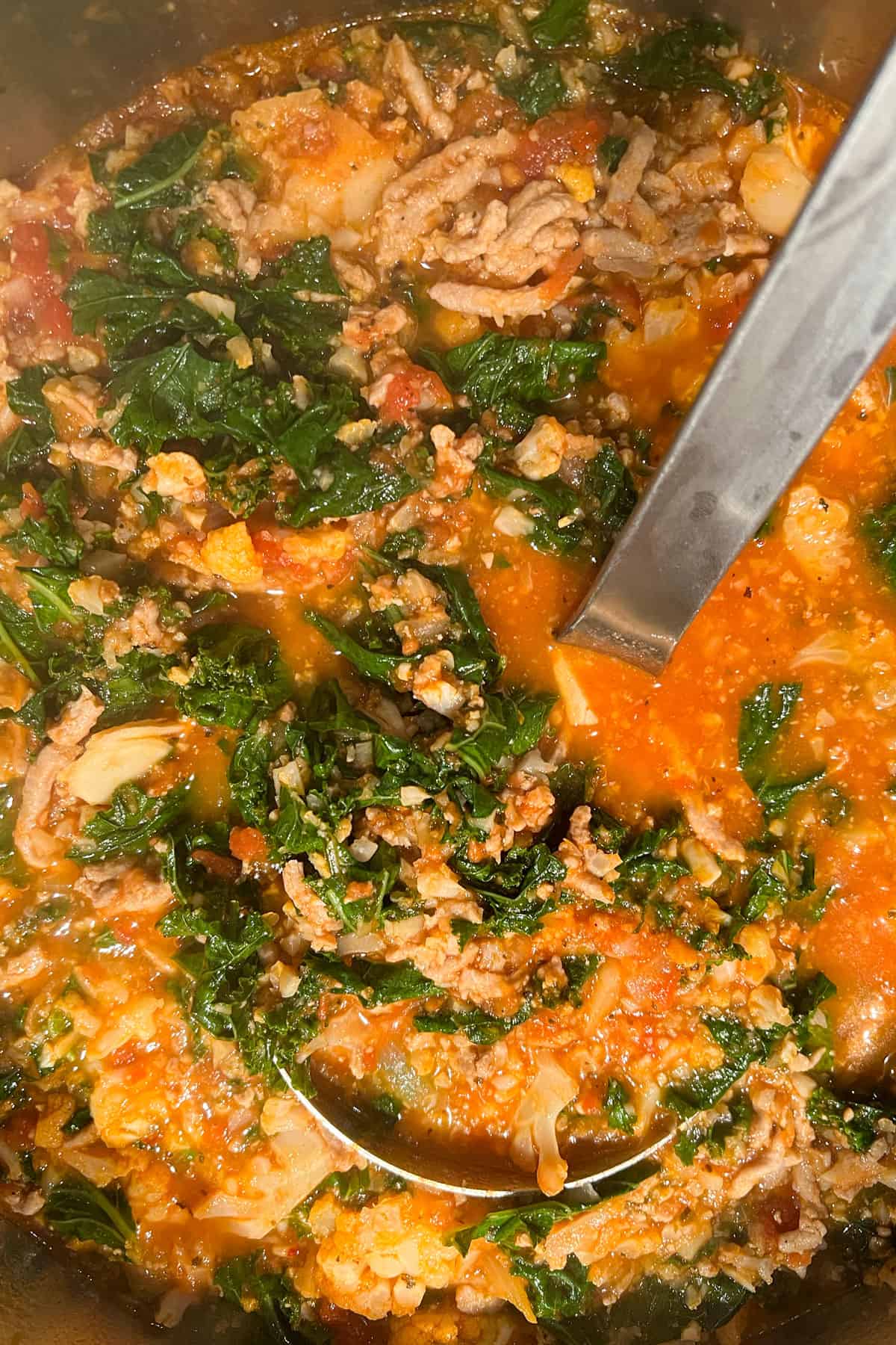 A ladle in a pot of ground turkey, kale, cauliflower soup with tomato broth.