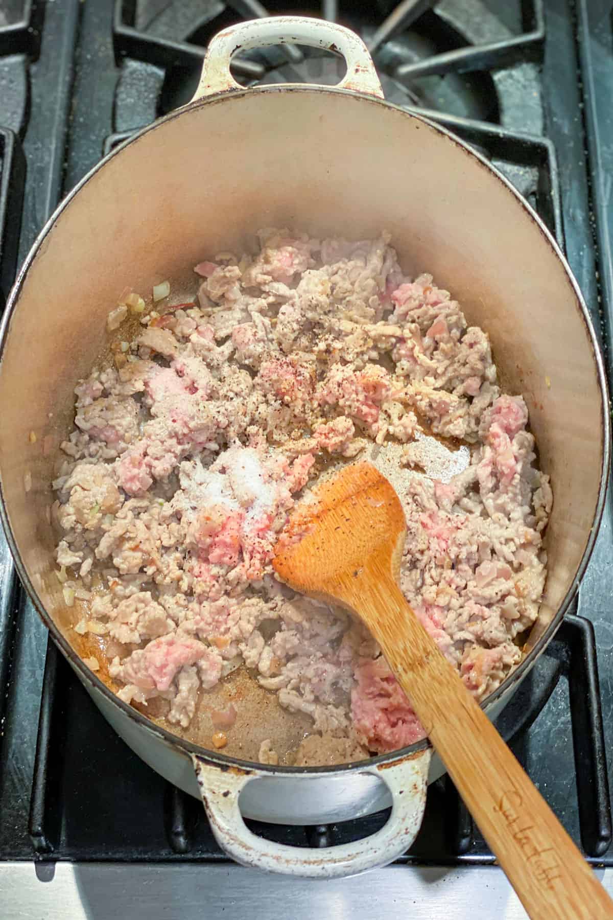 Partially cooked ground turkey being stirred and cooked in an oval dutch oven.