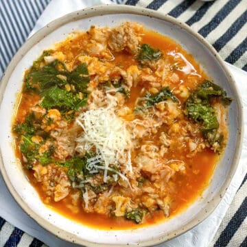 Ceramic bowl filled with ground turkey soup with kale, chopped cauliflower and tomato broth. Topped with grated parmesan.