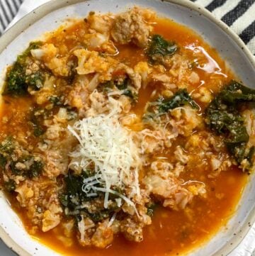 overhead shot of a white bowl filled with ground turkey vegetable soup and a heap of shredded parmesan in the middle.